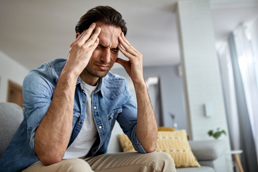 low angle view distraught man holding his head pain while sitting living room 1024x683